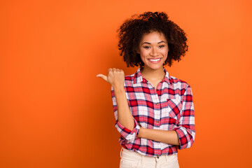 Portrait of attractive cheerful wavy-haired girl showing copy blank space ad isolated over bright orange color background