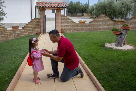 Image of a young dad preparing his daughter for the first day of school. Little girl with backpack and pink apron.
