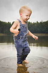 Small boy dressed in jeans playing with bark boat in lake