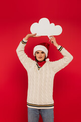 smiling young woman in santa hat and sweater holding thought bubble above head isolated on red.