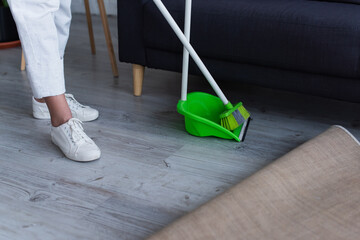 cropped view of woman in white sneakers near broom and scoop at home.