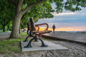 The Boardwalk on Balmy Beach in Toronto at daybreak with a park bench in the foreground and a...