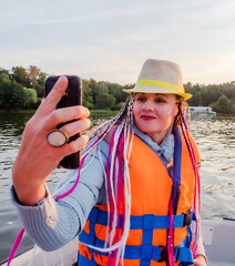 Woman taking picture of herself on smartphone during floating on kayak. Concept of rest, leisure and weekend. Middle Age Woman wearing life vests. Sunny autumn daytime.selective focus