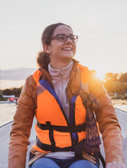 Beautiful brunette woman teen with glasses and in an orange life jacket rowing oars while sitting...