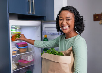 A young multi-racial woman unpacks her grocery shopping into the refrigerator