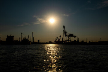 wejście do przemysłowego portu w Gdańsku. widoczne liczna żurawie i dźwigi na tle zachodzącego słońca - obrazy, fototapety, plakaty