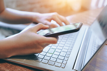 hand of person using smartphone with laptop on wooden table