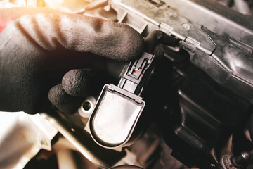 The auto mechanic is unplugging the ignition coil of the car engine in the engine compartment. - obrazy, fototapety, plakaty