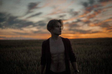 silhouette of a sexy muscular man at sunset in a field, a long-haired handsome man with a naked torso in nature. The concept of a romantic single man.