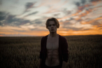 silhouette of a sexy muscular man at sunset in a field, a long-haired handsome man with a naked torso in nature. The concept of a romantic single man.