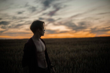 sexy man in a cardigan on a naked body with a rounded torso at sunset in a field.