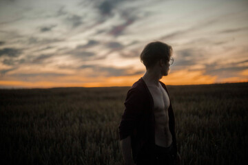 sexy man in a cardigan on a naked body with a rounded torso at sunset in a field.