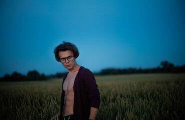 sexy man in a cardigan on a naked body with a rounded torso at sunset in a field.