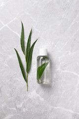 Cosmetic bottle with tonic water with leaves on marble background. Hyaluronic acid oil, serum with collagen and peptides skin care product. Mockup packaging, cosmetic design branding