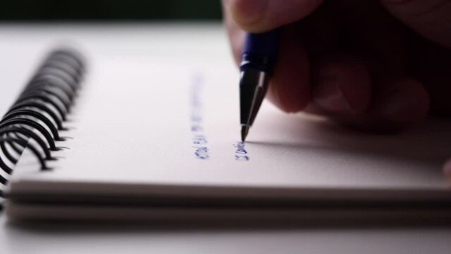 Concept of writing paper, letter, pen, notepad, diary. close-up man hand writing paper notebook with blue pen to note, memo, list action plan at office or home desk, selective focus 4k resolution
