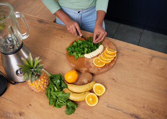 An overhead shot of a young woman preparing fruit and spinach for green smoothie