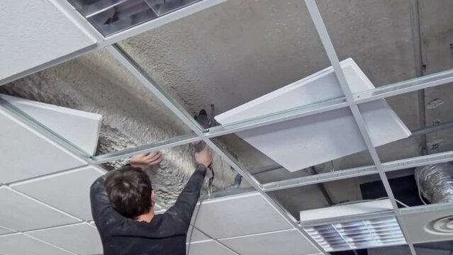 Construction worker performs a suspended ceiling maintenance with mineral fiber squares.