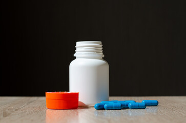 Plastic jar for pills. White jar with orange lid. The sterile container stands on the table. Cold medicine. Pharmaceutical activity. Multi-colored capsules with a medicinal substance.