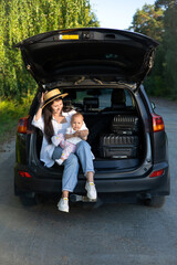 Car journey. Travel with a child by car. Mother and daughter sit in a car with an open trunk