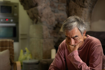 Grey hair man in his sixties, sitting in the sofa, serious, thinking very concentrated.