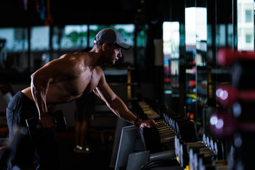 muscular man working out with dumbbells in gym dark tone,