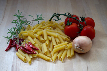Rohe Nuden Penne Tomaten Kräuter Gewürze auf einem Holzbrett gruppiert Zwiebel Rosmarinzweig frisch Chilischoten getrocknet