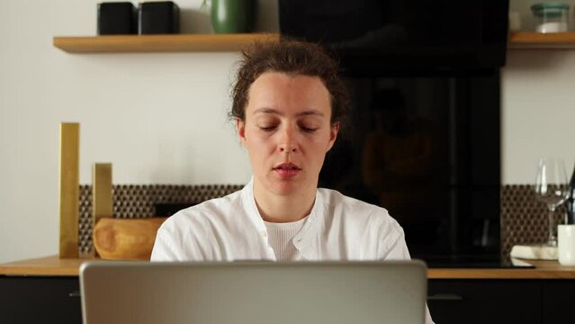 Young caucasian woman working on laptop doing remote freelance tasks,sitting in homeoffice,looking pensive,thinking of problems,solving business issues, wearing white shirt.Creative brainwork concept