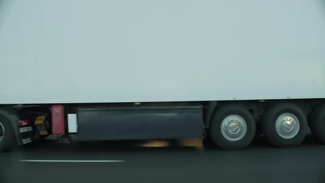 Car rides next to trailer of cargo lorry truck. Delivering logistic, freight. Import export concept. View through side window in motion. Speed on road. Maintaining a safe distance