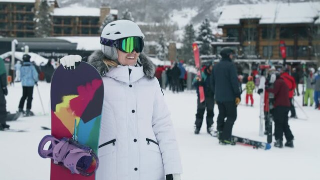 Girl having fun in Aspen waving hand to friends in slow motion. Happy young woman downhill the ski slope making a picture or video with snowboard at ski resort in snowy mountains enjoying vacation 6K