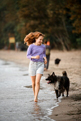 Naklejka na ściany i meble Barefoot young woman having fun and runs with the dog along the shore