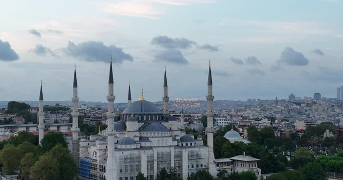 Establishing orbiting aerial drone shot of a Hagia Sophia Holy Grand Mosque with Bosphorus bridge and city skyline with a flag on the background in Fatih, Istanbul, Turkey at sunset.