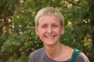 Young woman with a short hairstyle with a nose piercing laughs joyfully in the forest  on green...