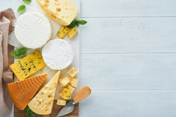 Set or assortment cheeses. Maasdam, smoked cheese, camembert, blue cheese, parmesan, brie cheese with basil and pepper on on white marble board white wooden old background. Top view. Free copy space.