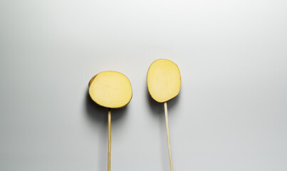 two pieces of potato stuck on a stick on a gray background