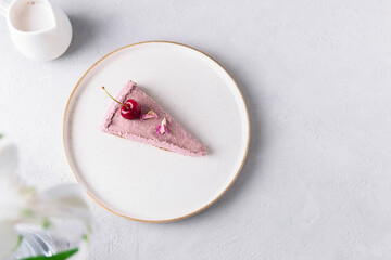 Top view of a slice of a raw cherry cake on white plate on a neutral grey background. Healthy raw dessert