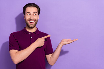 Photo of impressed young brunet guy hold index look empty space wear violet t-shirt isolated on purple color background