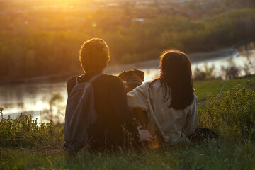 young people in love a guy and a girl are sitting in nature on a high bank of the river with their pet big dog at sunset outside the city