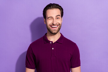 Photo of impressed young brunet guy wink wear purple t-shirt isolated on violet color background