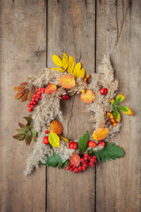 Floral autumn door wreath from natural materials: colorful  berries, rowan, dry flowers and apples on wooden background. Fall flower decoration workshop. Top view.