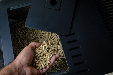 hand holding wood pellets going into the stove compartment, alternative heating energy solution