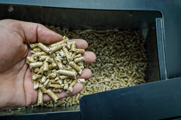 hand holding wood pellets going into the stove compartment, alternative heating energy solution