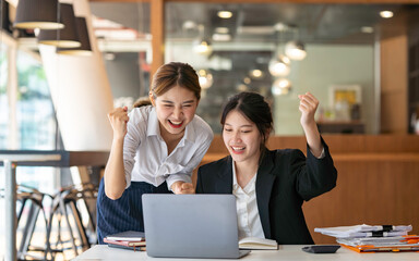 Asian businesswoman rejoicing and raising her hand, working and using a laptop Document graph showing the results in the meeting room.