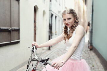 Fototapeta na wymiar City Cycling: Blonde Girl Posing with Bicycle in Front of Urban Buildings, Embracing an Active Lifestyle