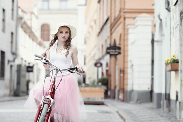 Fototapeta na wymiar City Cycling: Blonde Girl Posing with Bicycle in Front of Urban Buildings, Embracing an Active Lifestyle