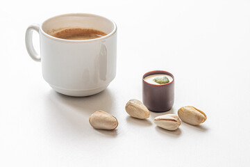 chocolate candy with creamy pistachio filling, pistachios and a cup of coffee on white surface