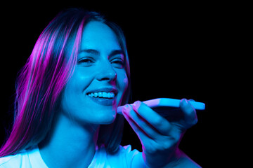 Obraz premium Closeup happy young pretty girl with cellphone isolated on dark background in purple neon light. Concept of emotions, facial expression, youth, aspiration.