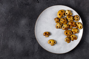 Round plate with mushrooms in the form of skulls and fork on white table. Edible Halloween Concept
