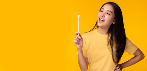 Happy woman brushing beauty tooth using toothbrush Young lady has beauty teeth Beautiful asian girl get strong tooth white teeth and nice tooth alignment Yellow background, copy space Dental care