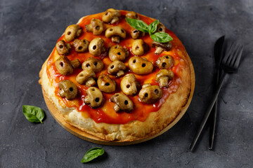 Homemade pizza with tomato sauce and mushrooms in the form of skulls. Concept for Halloween celebrations