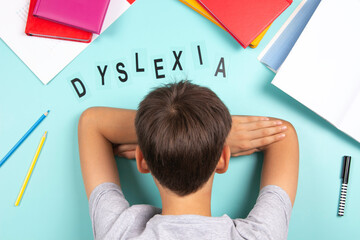 Sad tired frustrated boy lies on the table with many books. Word Dyslexia on light blue background....